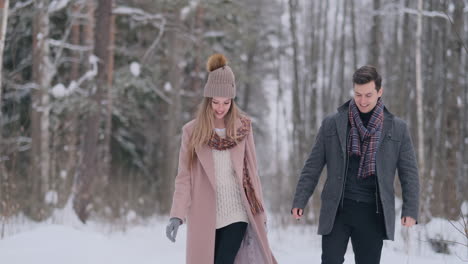 In-the-winter-snowy-forest,-young-men-and-women-dressed-in-coats-and-scarves-are-walking-and-having-fun.-Loving-couple-spend-together-valentines-day.
